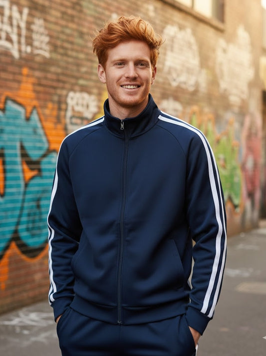 Man wearing a navy tracksuit with white stripes standing in front of a graffiti-covered wall.