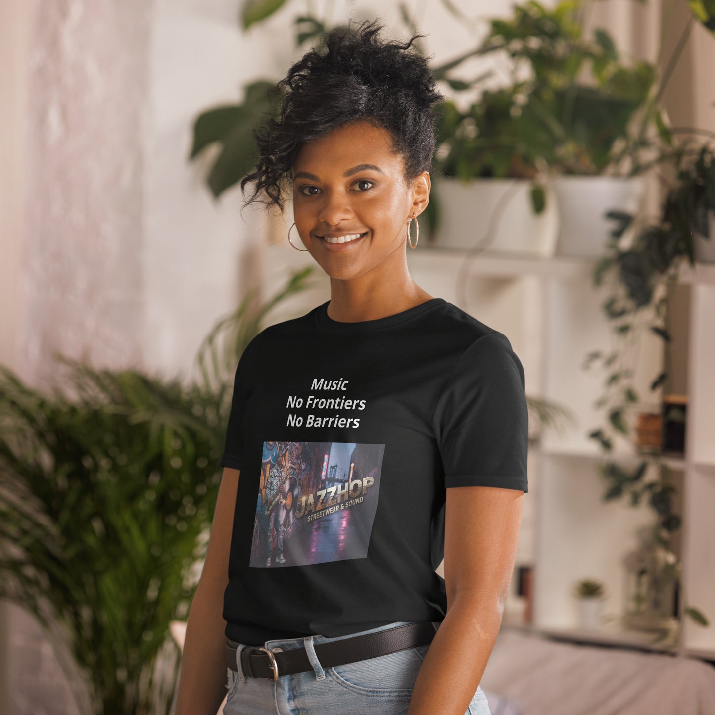 Person wearing a black t-shirt with text and a graphic design, standing in a room with plants.